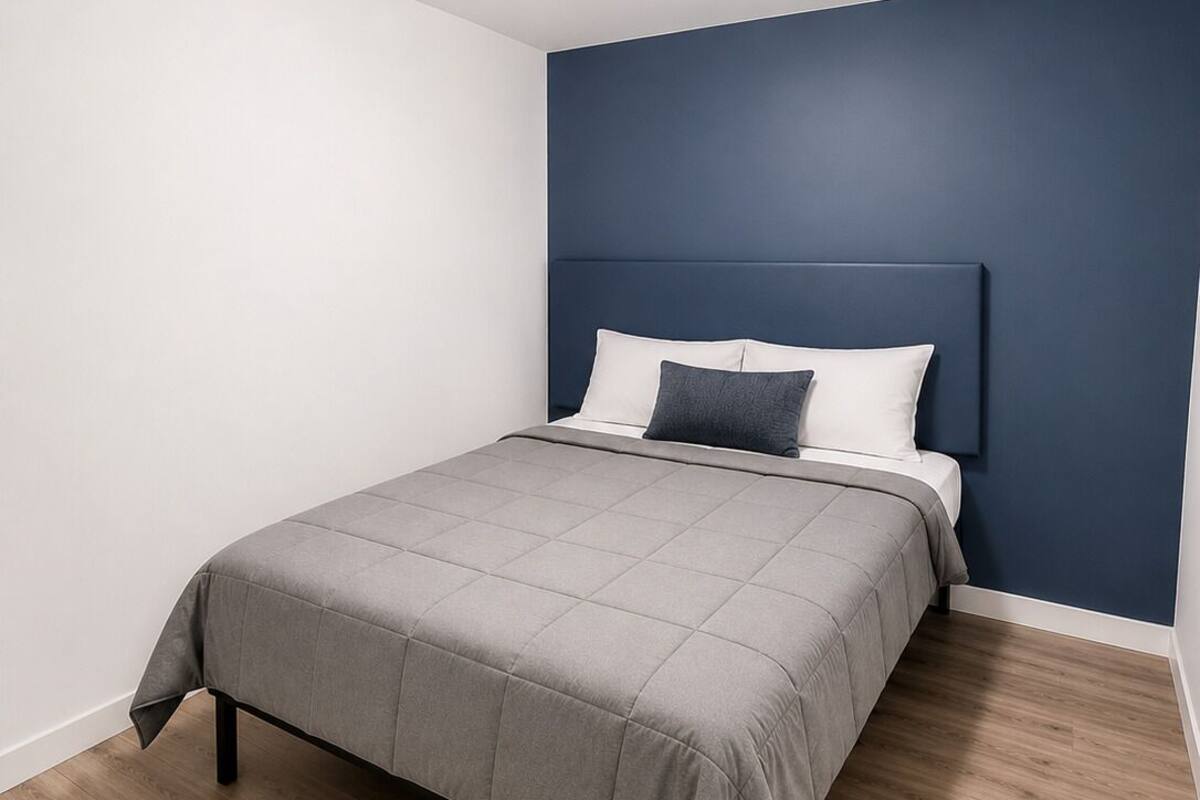 A bedroom with a bed, a headboard, a ceiling light, and wooden flooring.