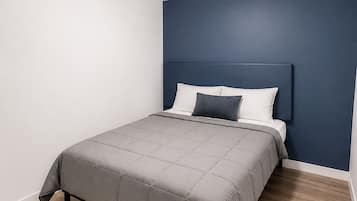 A bedroom with a bed, a headboard, a ceiling light, and wooden flooring.