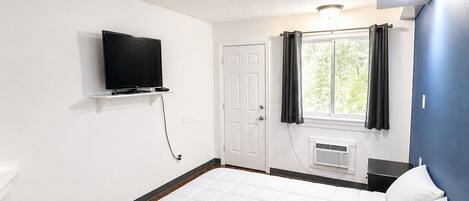 A hotel room with a bed, a TV mounted on the wall, a window with curtains, and a ceiling light.