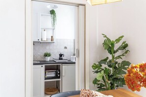 Una cocina compacta con armarios blancos, un microondas, una cafetera y una planta en maceta.