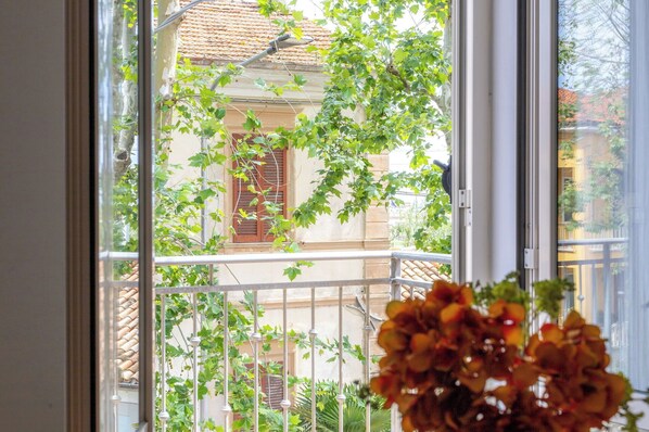 A window with a view of a building with a tiled roof and a balcony with a metal railing.
