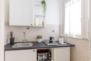 Una cocina con un lavamanos, estufa, microondas y ventana con cortinas.