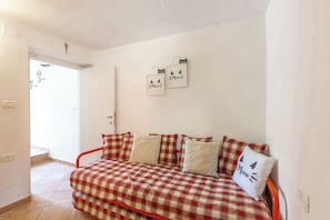 Una habitación con un sofá a cuadros, una puerta con una cruz encima y dos cuadros colgados en la pared con diseños de gatos.