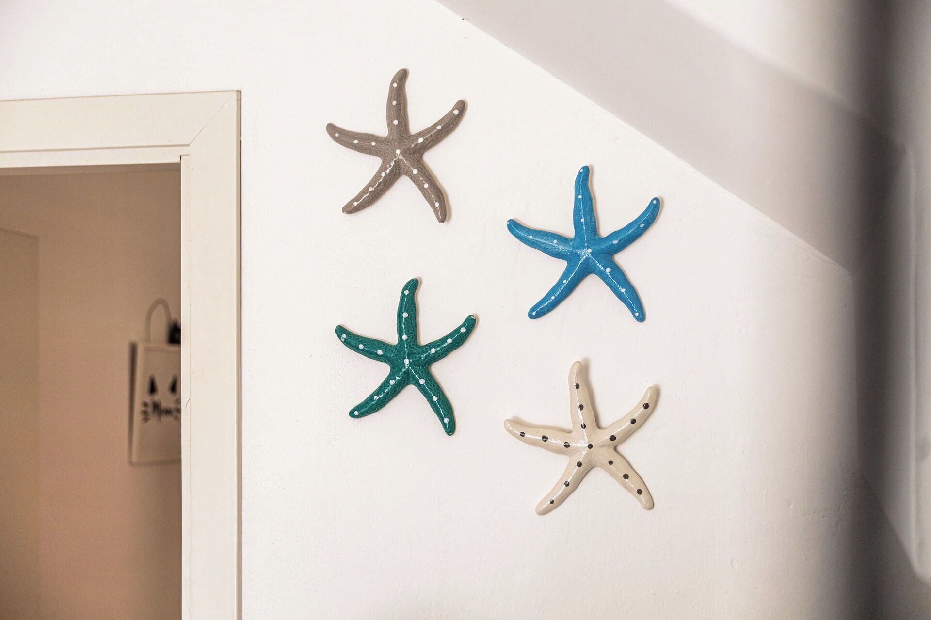 Cuatro adornos con forma de estrella de mar sobre una pared blanca.