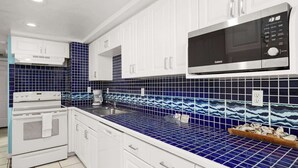 Cocina con armarios blancos, microondas y azulejos azules estampados.