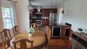 Un coin repas avec une table et des chaises en bois, un lustre, et une cuisine dotée de meubles et d’appareils électroménagers en bois.