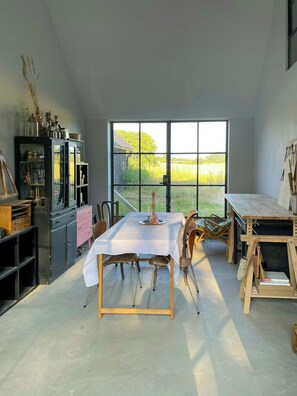 A dining area with a table, chairs, and a view of a field through large windows. - Renovated Scanian farmhouse with two studios (Skåne tranås)