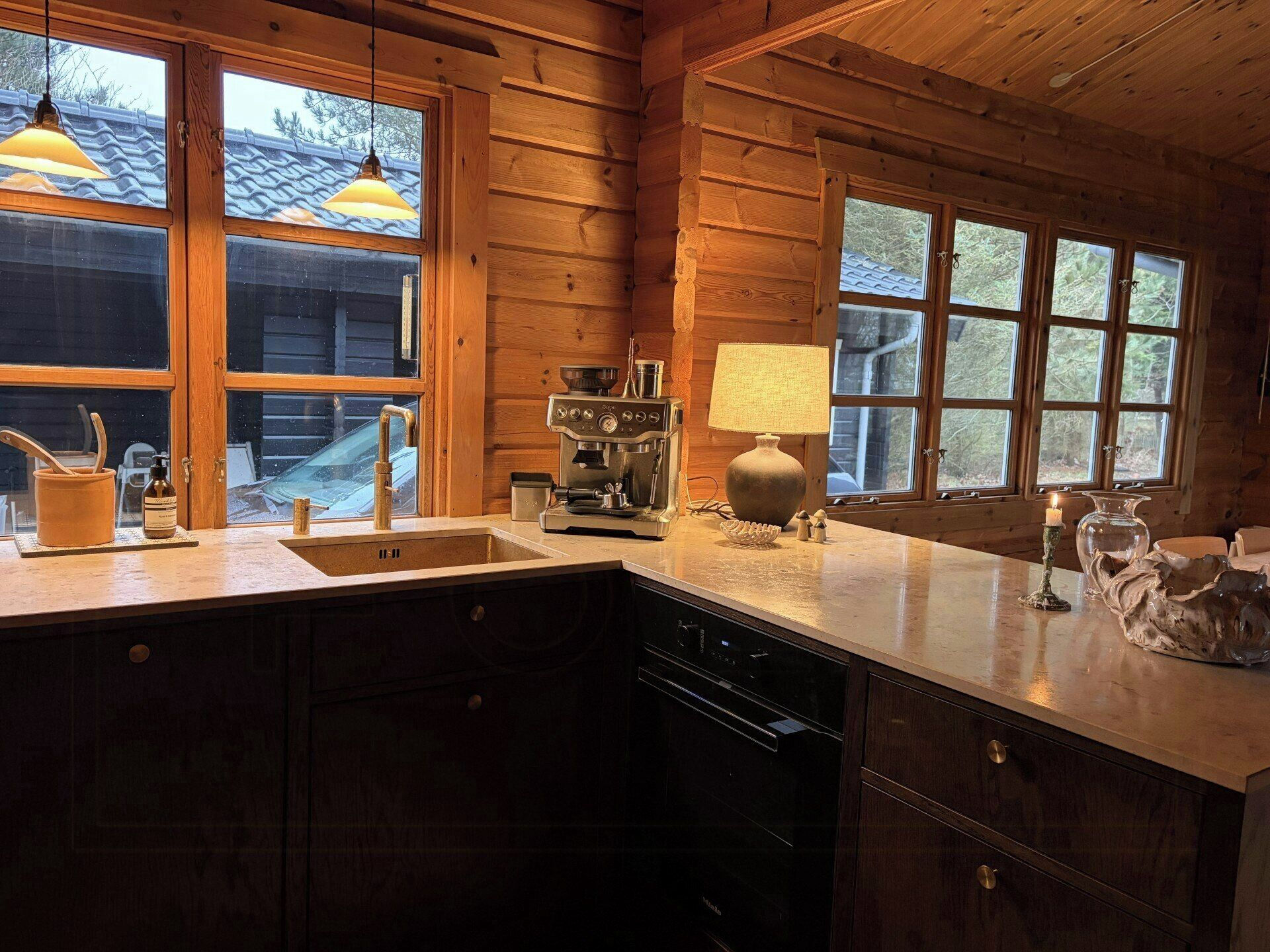 A wooden cabin kitchen with a large window, a coffee maker, and a lamp.