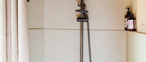 Ducha con cabezal de ducha de mano, grifo de mano y panel de control en la pared.