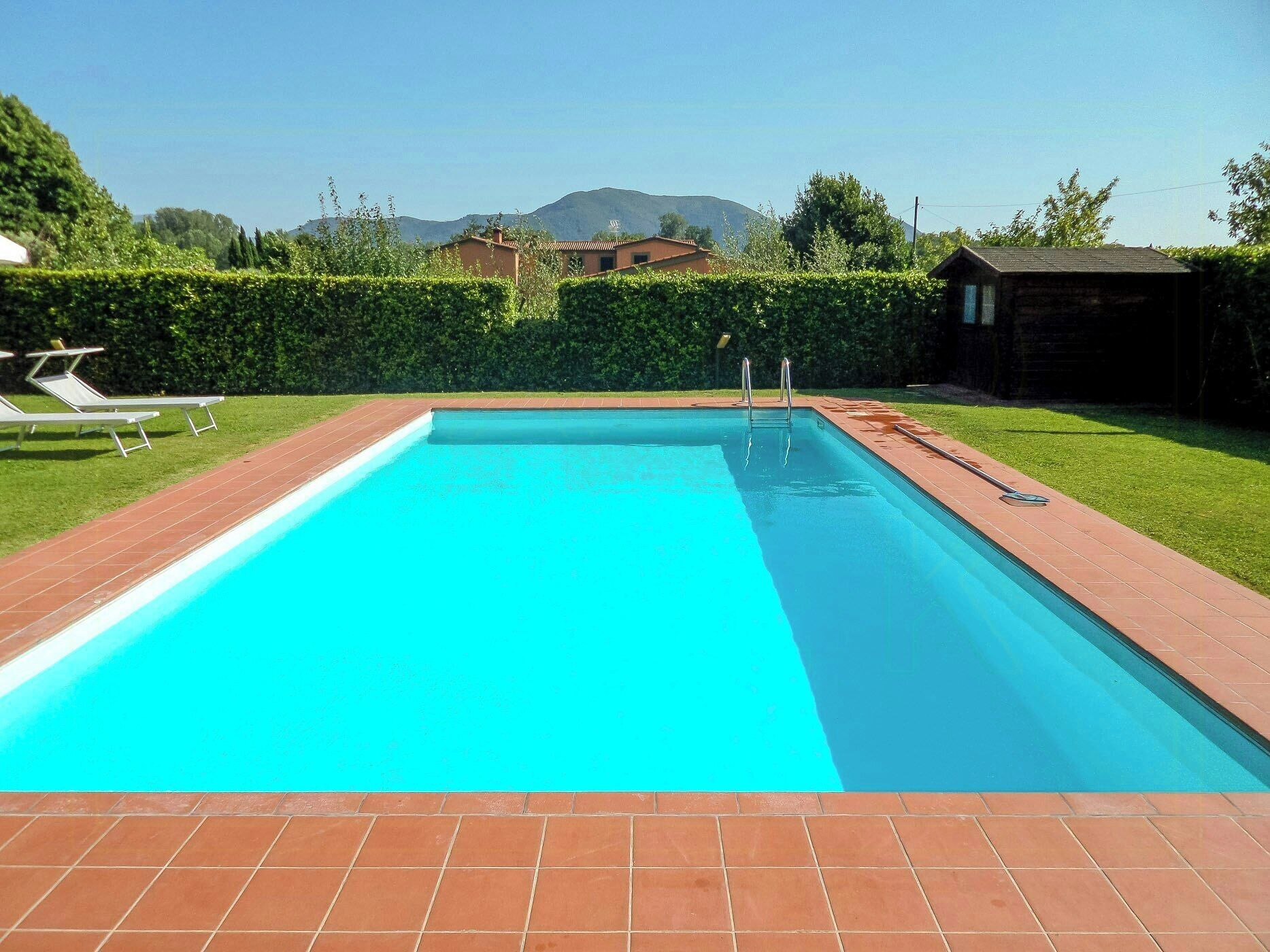 A rectangular swimming pool with a clear blue water surface, surrounded by a brick deck.