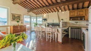 Una cocina amplia con armarios de madera, un comedor con sillas blancas y vistas a través de la puerta abierta.