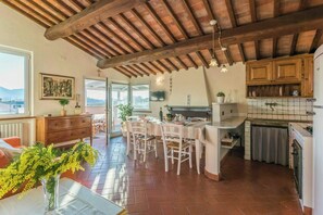 A spacious kitchen with wooden cabinets, a dining area with white chairs, and a view through the open door. - Apartment with private pool near Lucca (Lucca)