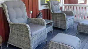 Eine überdachte Veranda mit Korbmöbeln, darunter zwei Stühle und ein kleiner Tisch.