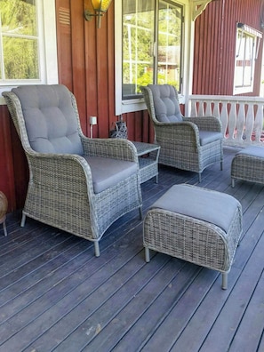 Eine überdachte Veranda mit Korbmöbeln, darunter zwei Stühle und ein kleiner Tisch.