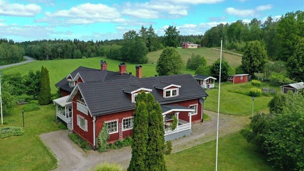 Ein rotes Haus mit einer großen Garage, umgeben von grünen Feldern und Bäumen.