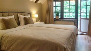 Ein Doppelbett mit Kopfteil, ein Nachttisch mit Lampe und ein Fenster mit Vorhängen.