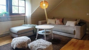 Ein gemütliches Wohnzimmer mit Sofa, Hocker, kleinem runden Tisch und einer Pendelleuchte.