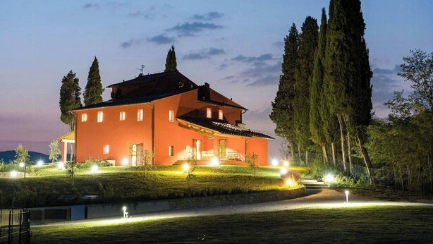 A large, two-story building with a red facade, multiple windows, and a well-lit entrance. - Family apartment with pool in estate in Valdarno (Reggello)
