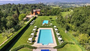 A pool area with two rectangular pools, surrounded by lounge chairs and umbrellas, set in a lush green landscape with a view of distant hills. - Family apartment with pool in estate in Valdarno (Reggello)
