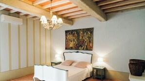 A bedroom with a bed, two bedside tables with lamps, a chandelier, a large painting on the wall, and a tiled floor. - Family apartment with pool in estate in Valdarno (Reggello)