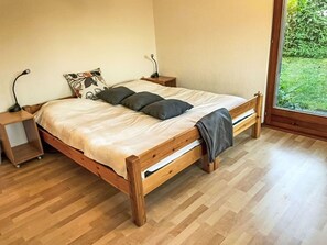 Un lit en bois avec une tête de lit, deux tables de chevet et une fenêtre donnant sur un paysage verdoyant.