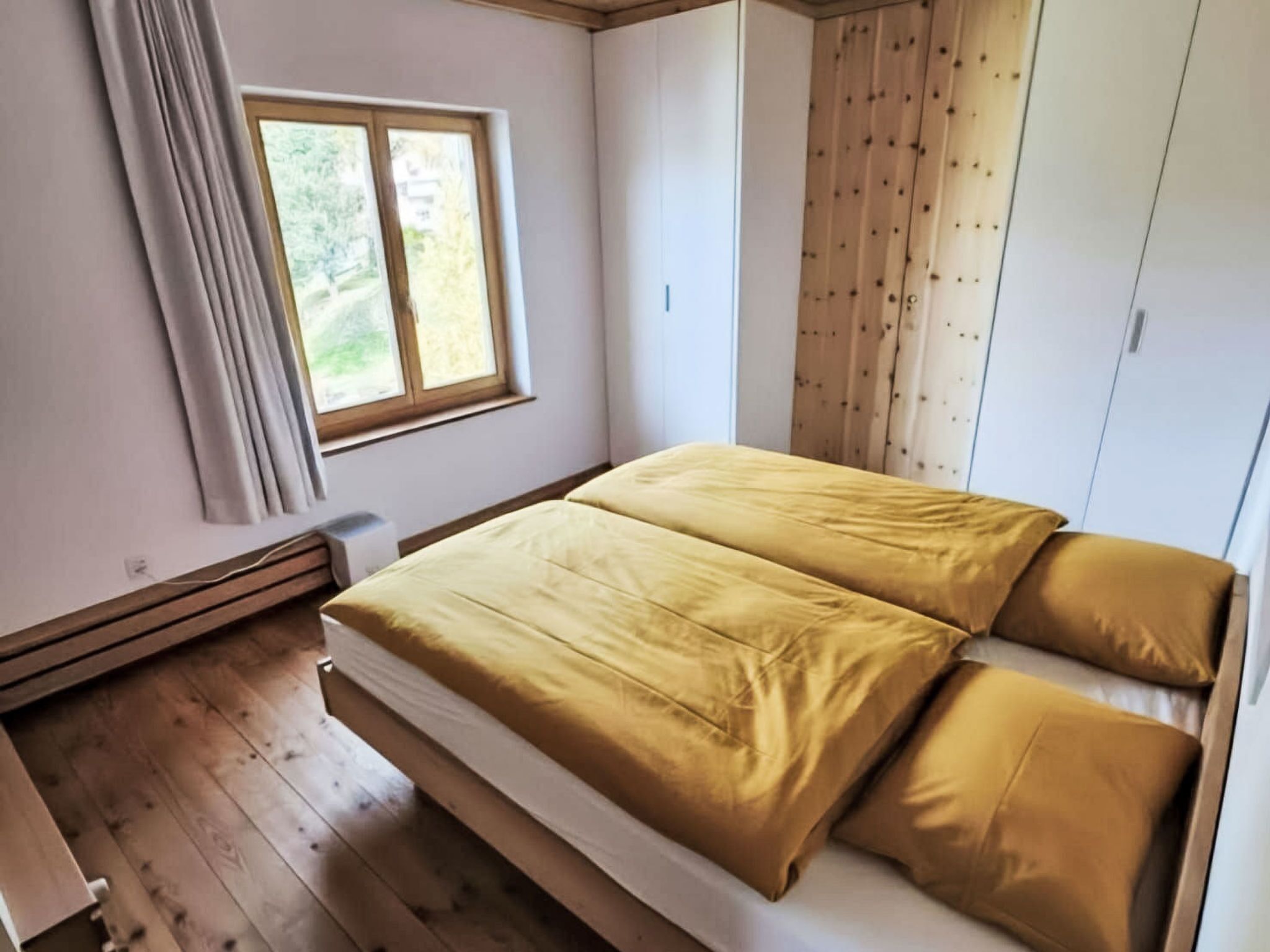 Quarto com cama, janela, piso de madeira e guarda-roupa.
