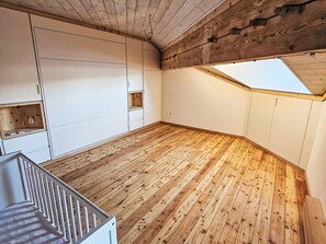 Ein Zimmer mit Holzboden, weißen Wänden, eingebauten Stauraumschränken, einer schrägen Decke mit Oberlicht und einer weißen Treppe.