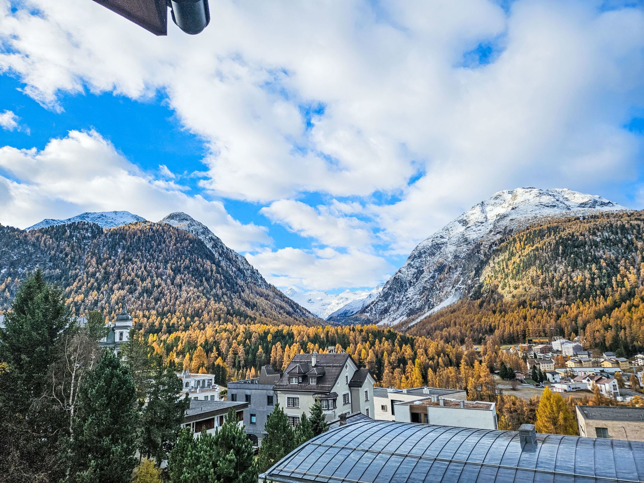 A mountainous landscape with a town nestled in the valley, featuring buildings with flat roofs and a prominent greenhouse structure.