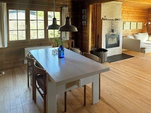 Un interior de madera con una mesa de comedor, sillas, un jarrón azul, una chimenea y un sofá.