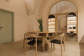 Un coin repas avec une table ronde, quatre chaises, un vase avec des plantes et une cloison en bois avec des étagères en arrière-plan.