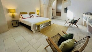 Ein Schlafzimmer mit einem Bett, Nachttischen, einem Sessel, einem kleinen Tisch und einer gewölbten Tür.