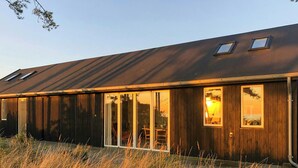 A modern building with a sloped roof, large sliding glass doors, and a small window. - Unspoiled view to the sea and wild nature (Store Fuglede)