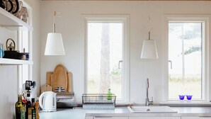 A modern kitchen with white cabinetry, a large island, pendant lights, and a view through the windows. - Unspoiled view to the sea and wild nature (Store Fuglede)
