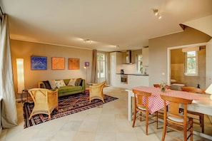 A living room with a sofa, chairs, a dining table with checkered tablecloths, and a kitchen area with cabinets and a stove.