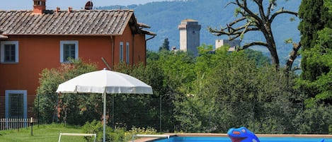 A swimming pool with inflatable toys, a white umbrella, and a chair.