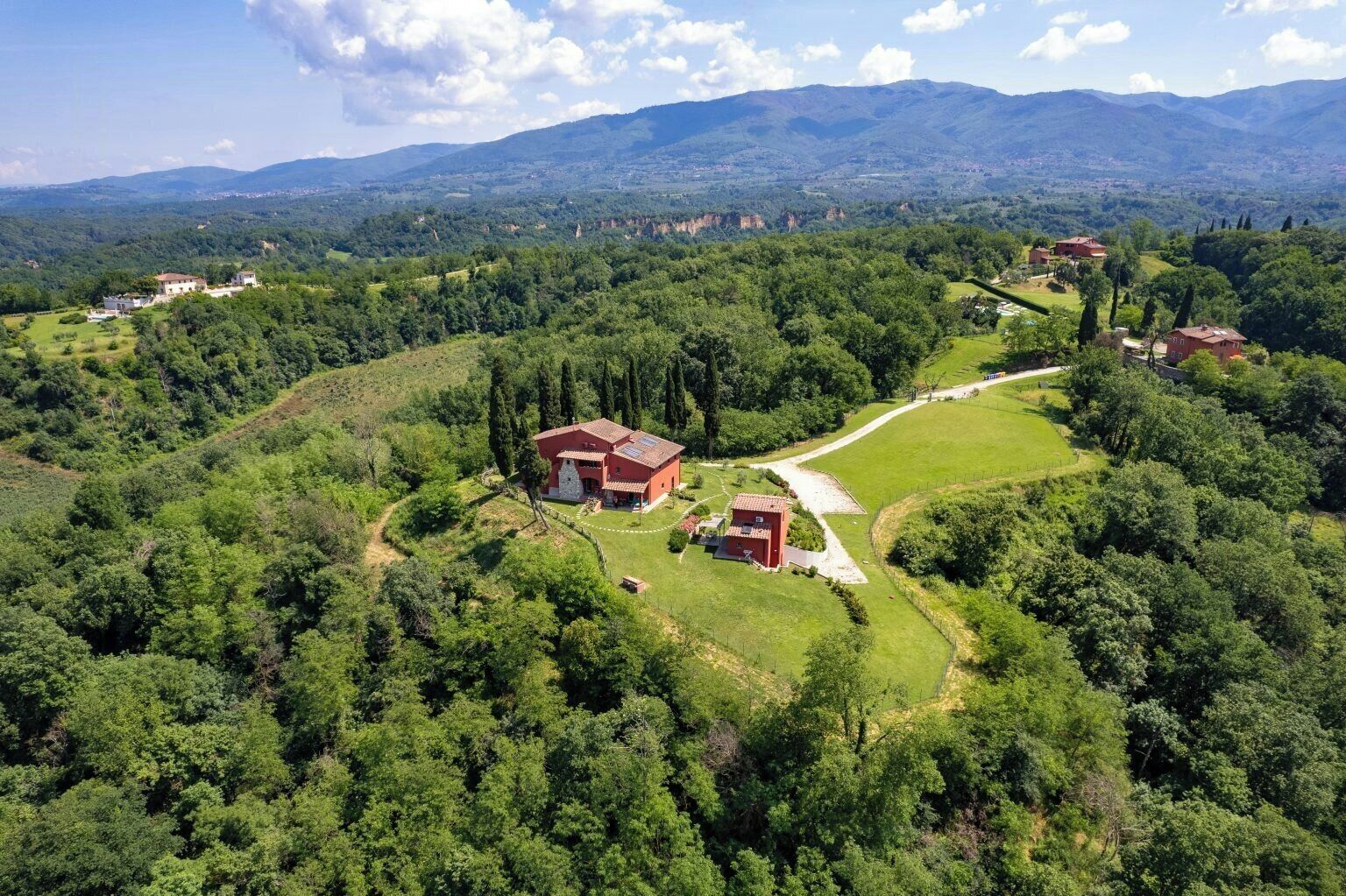 An aerial view of a rural property with multiple buildings, surrounded by lush greenery and mountains in the background.