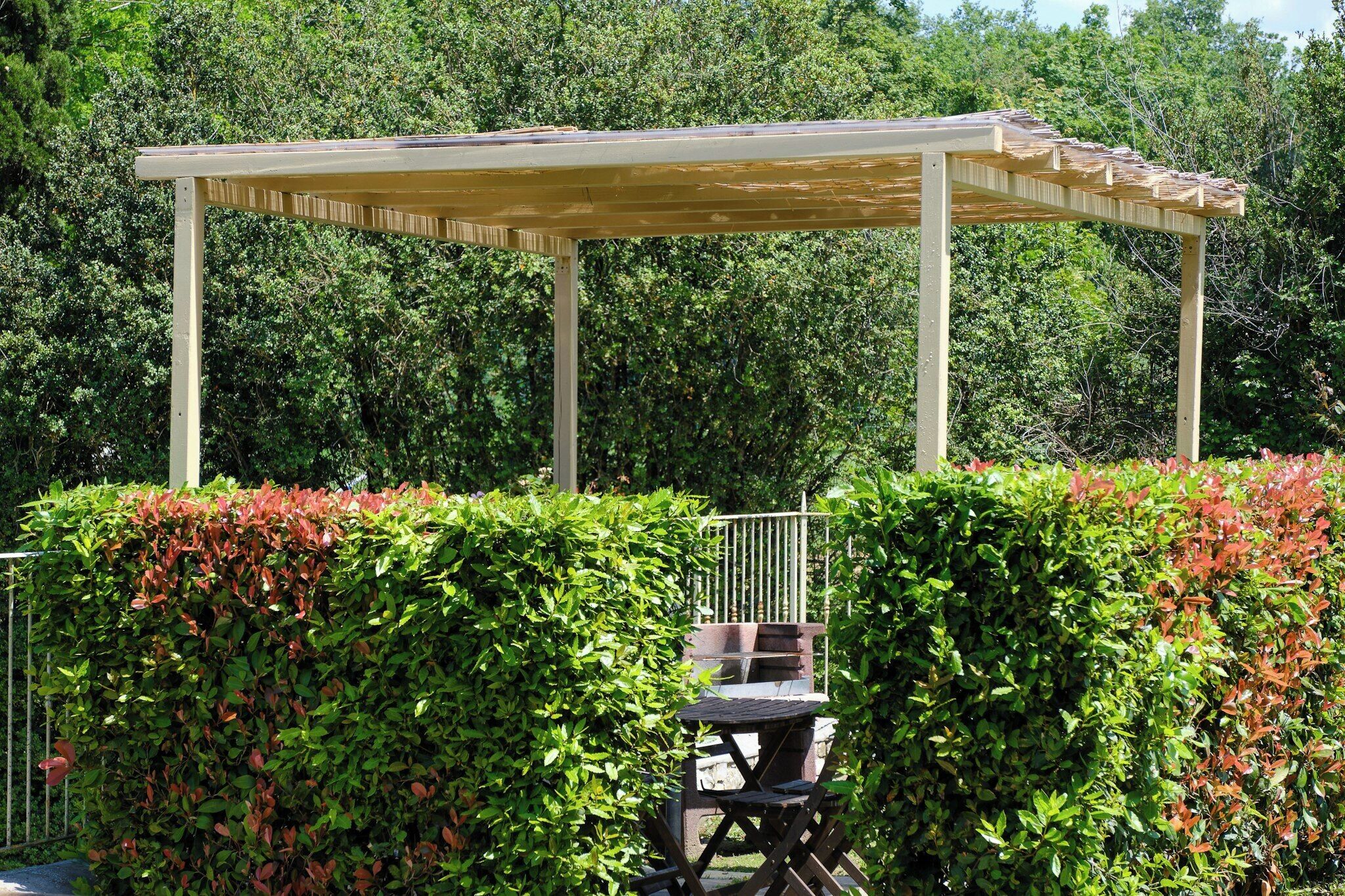 Une structure en forme de pergola, avec une table et des chaises en dessous, entourée d’un feuillage verdoyant et luxuriant.