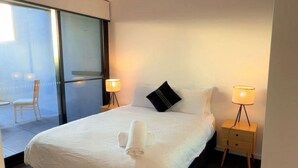A modern hotel room with a large bed, two bedside lamps, a small bedside table, and a view through a glass door to an outdoor area. - Cozy2BR free parking, @Woden, pet alow (Phillip)