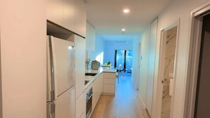 A narrow hallway with a kitchen on one side, a dining area with a table and chairs, and a bathroom visible through an open door. - Cozy2BR free parking, @Woden, pet alow (Phillip)