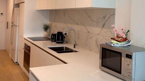A modern kitchen with white cabinetry, a marble backsplash, a built-in microwave, and a bar area with stools. - Cozy2BR free parking, @Woden, pet alow (Phillip)