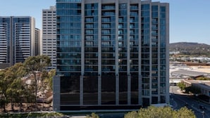 A modern high-rise building with a grid of windows, surrounded by trees and other buildings. - Cozy2BR free parking, @Woden, pet alow (Phillip)