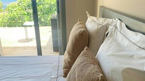 A bed with white bedding and two beige pillows, a window with a view of greenery and mountains, and a metal table in the foreground. - Villa with sea view and garden in Corsica (Porto-Vecchio)
