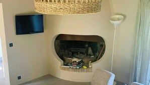 A living room with a fireplace, a television, and a coffee table with books and a decorative item. - Villa with sea view and garden in Corsica (Porto-Vecchio)