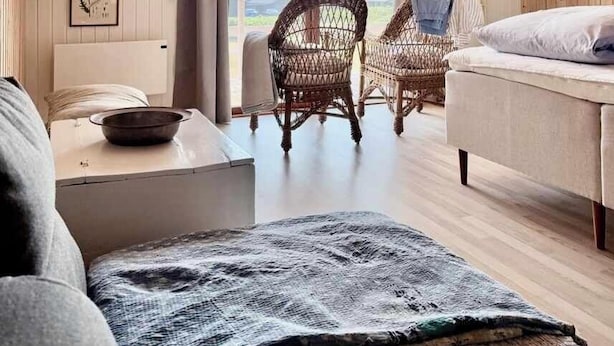 A cozy loft bedroom with a sloped ceiling, a large window, two wicker chairs, a bed, and a small table with a bowl. - Cozy summer house in Agger near the North Sea (Vestervig)