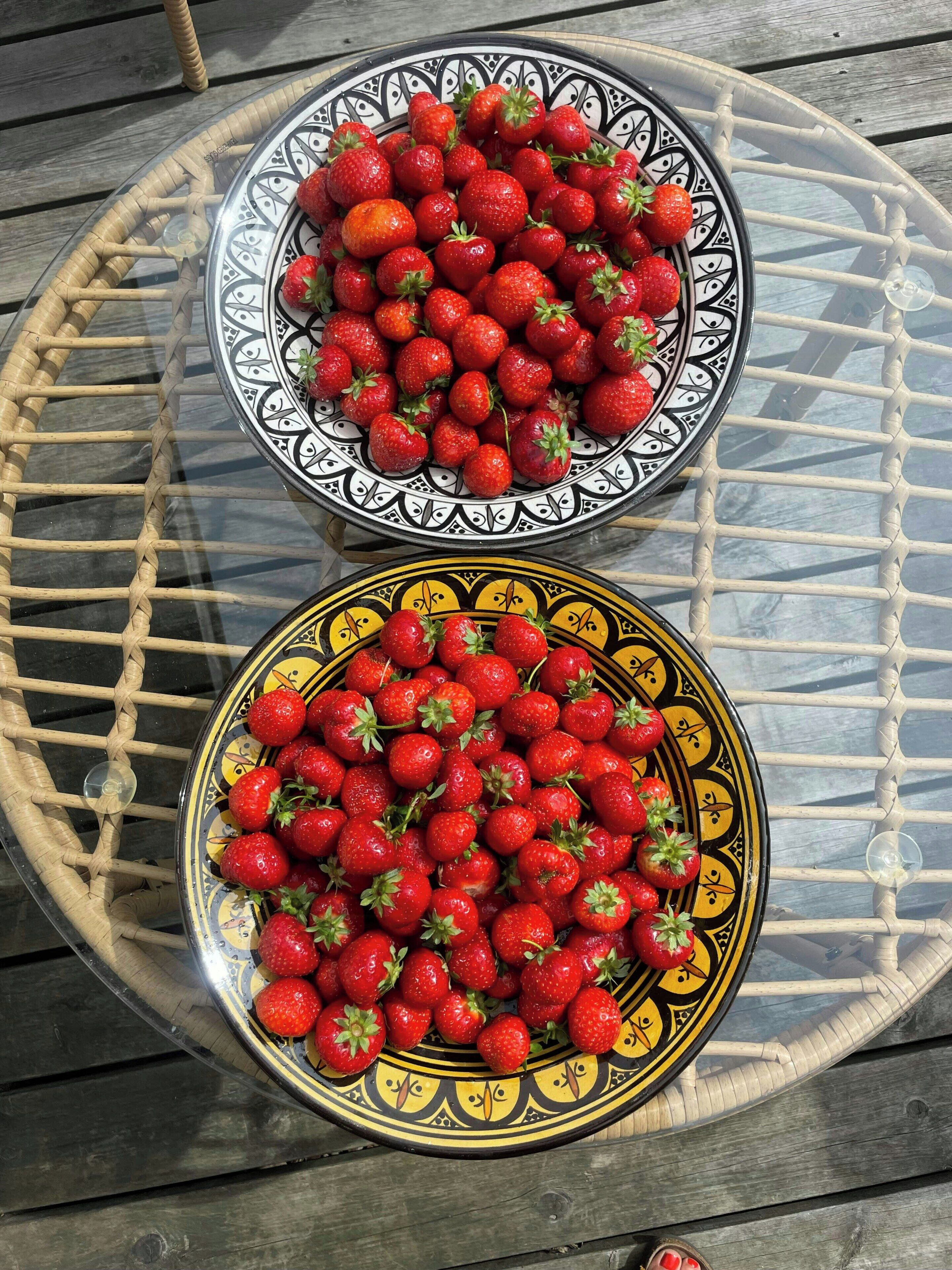 Deux assiettes de fraises sur une table en verre dont le plateau est fait d’un matériau tressé.