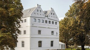 En stor, hvid bygning med flere etager, symmetrisk arkitektur, store vinduer og et markant kors på taget.