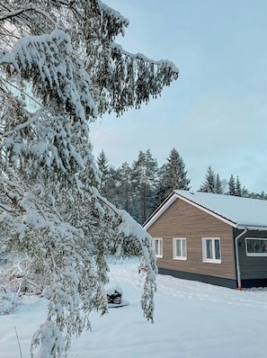 Eine Holzhütte mit schneebedecktem Dach, umgeben von immergrünen Bäumen.