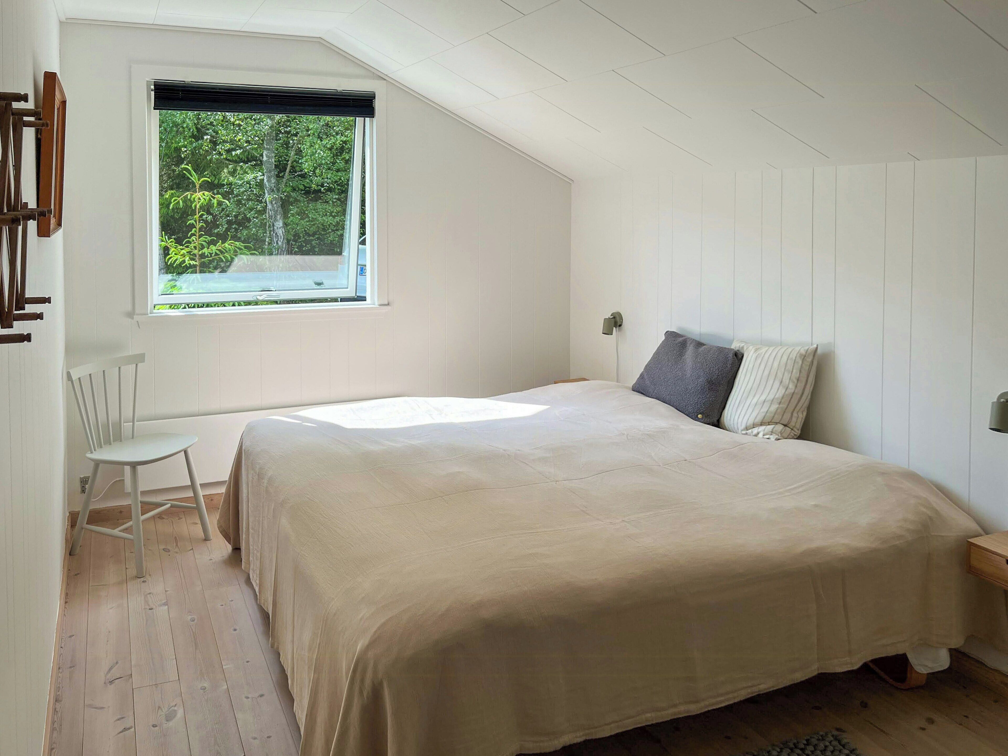 Ein Schlafzimmer mit einem großen Bett, einem Fenster mit Blick ins Grüne, einem weißen Stuhl und Holzboden.