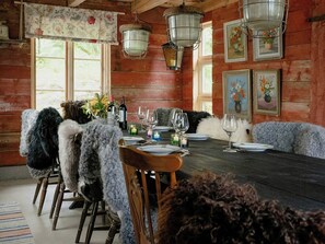 A rustic dining room with wooden walls, a wooden dining table set for four, and a chandelier. - Country life near city and lake with room for many (Torestorp)