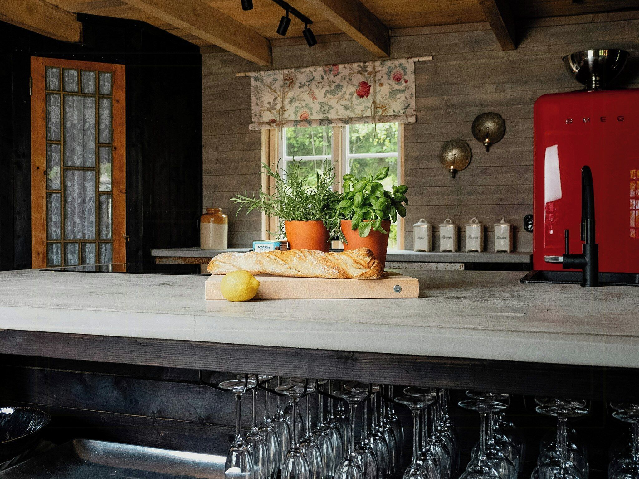 A kitchen with a wooden countertop, a red appliance, and a window with a floral valance.